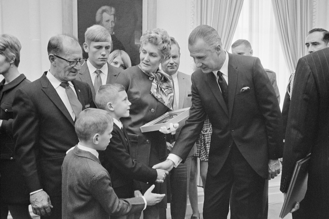 A man shakes hands with a young boy as his family stands around him.