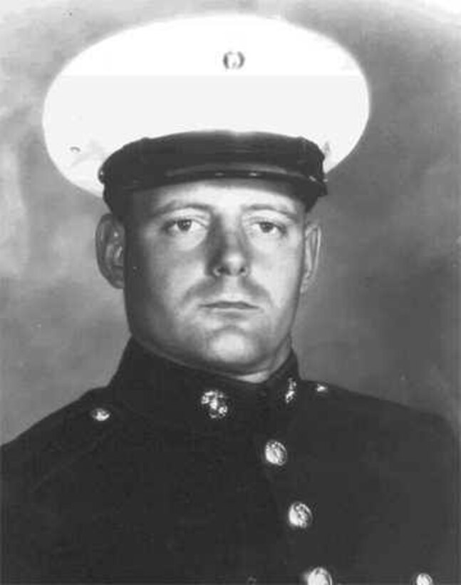 A man in uniform and cap looks forward.