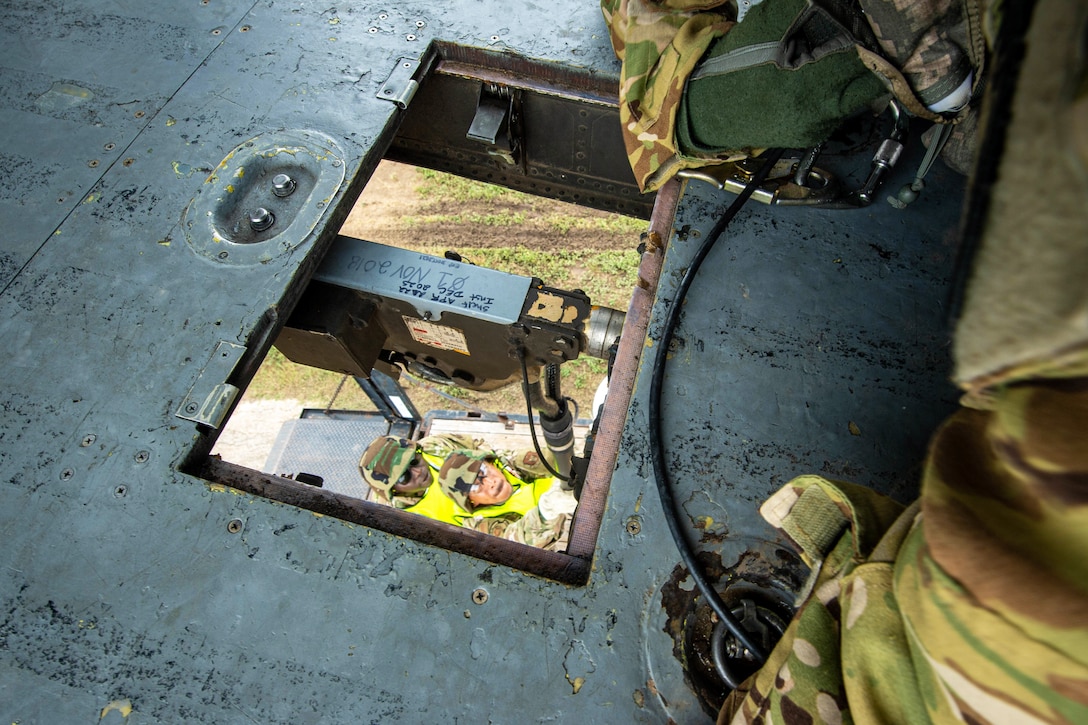 Two airmen on the ground attach a rope to a hovering helicopter.