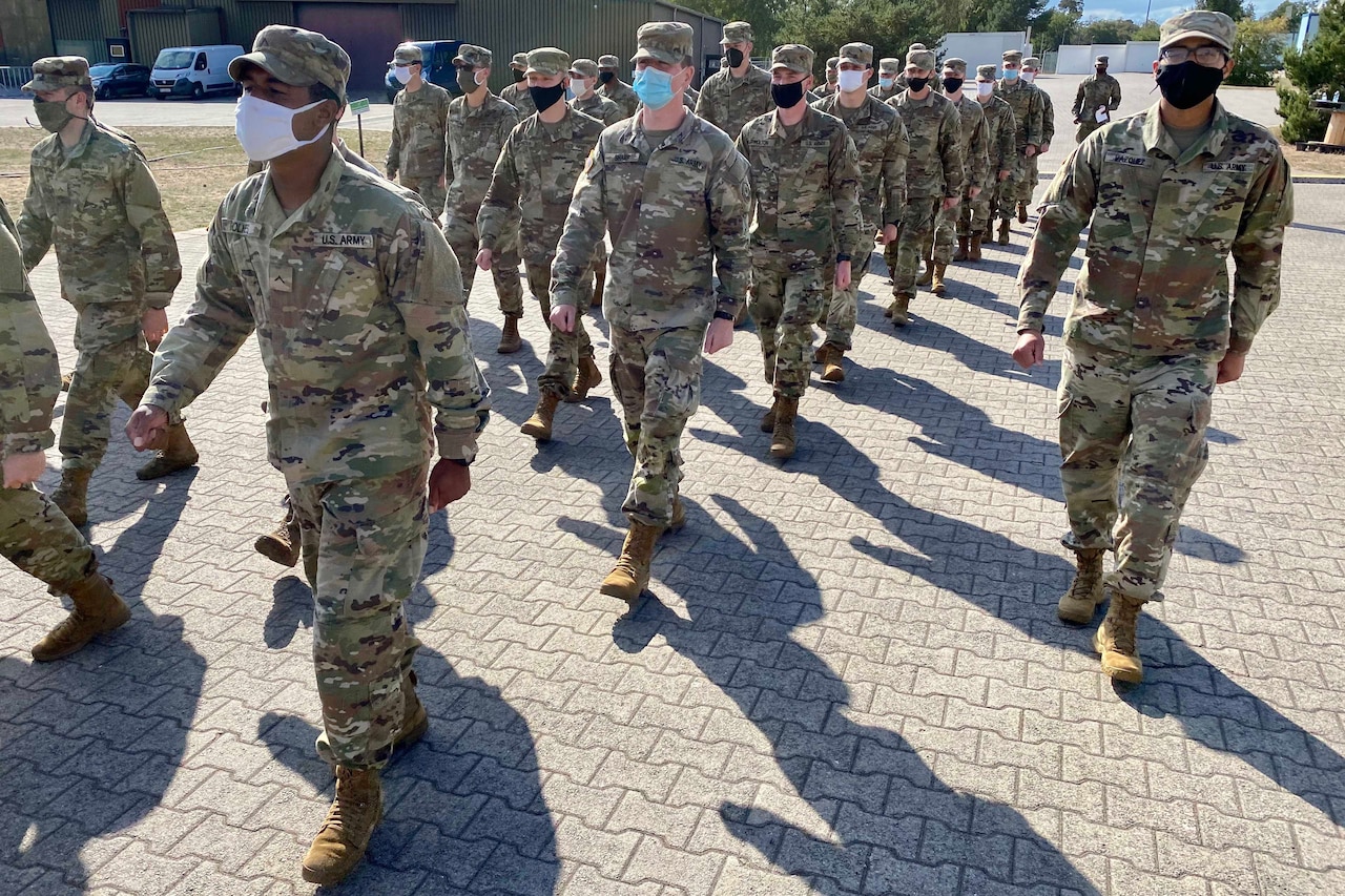 Soldiers wearing face masks march as a group.