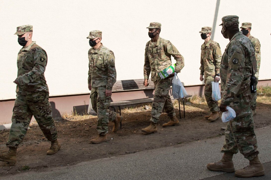 Soldiers wearing face masks picking up items.