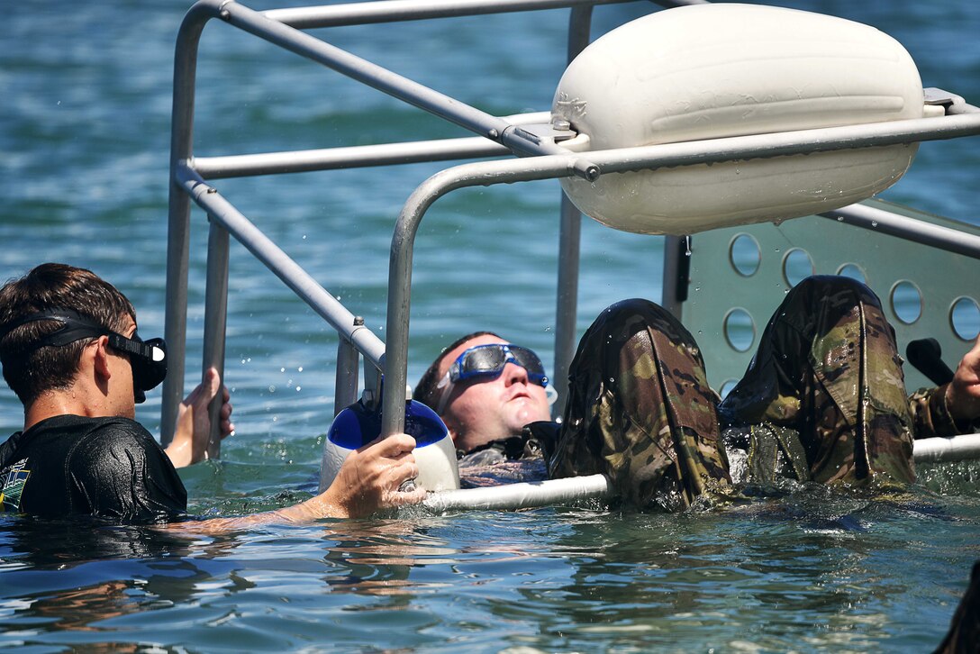 A service member moves another in underwater equipment during a water exercise.