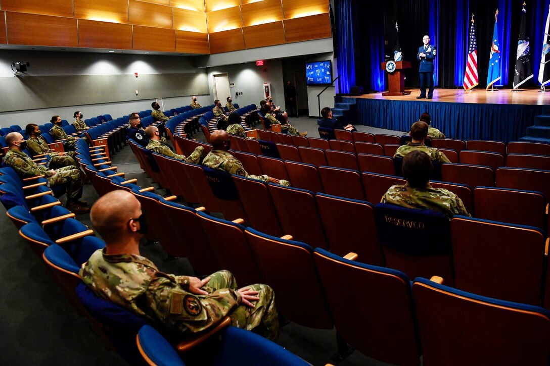 A man in a military uniform stands on stage and speaks to an audience.