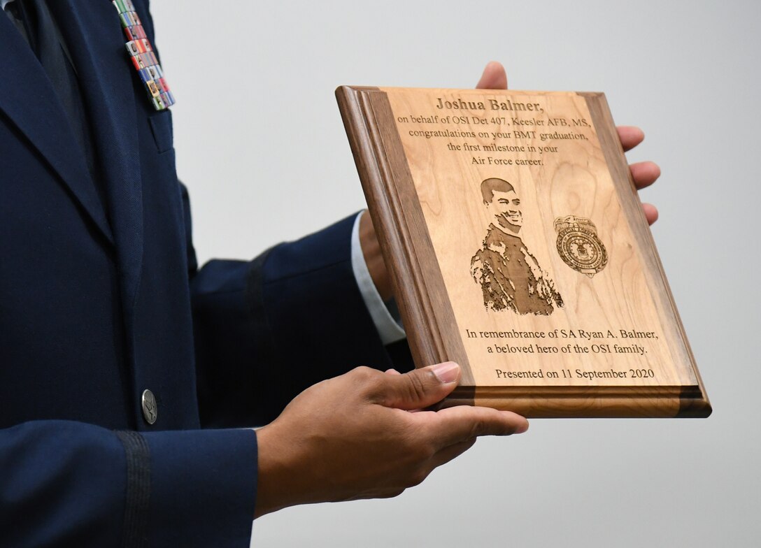 U.S. Air Force Special Agent Shannon Robinson, Air Force Office of Special Investigations Detachment 407 commander, holds a plaque during a presentation ceremony inside the Levitow Training Support Facility at Keesler Air Force Base, Mississippi, Sept. 11, 2020. Airman Joshua Balmer, 737th Training Group basic military training graduate and son of fallen OSI Special Agent Ryan Balmer, was presented mementos by the detachment following his graduation from BMT. (U.S. Air Force photo by Kemberly Groue)