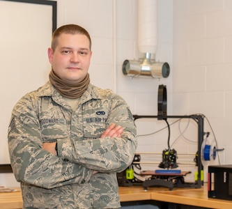 Staff Sgt. John Woodward, a metals technician with the 157th Maintenance Group, poses with a 3D printer, Pease Air National Guard Base, N.H, Sept. 3, 2020. Woodward used his background and education in metals technology to advance his shop’s use of the 3D printer, allowing technicians to create prototypes, plastic tools and molds for crafting multifaceted equipment. (U.S. Air National Guard photo by Staff Sgt. Victoria Nelson)