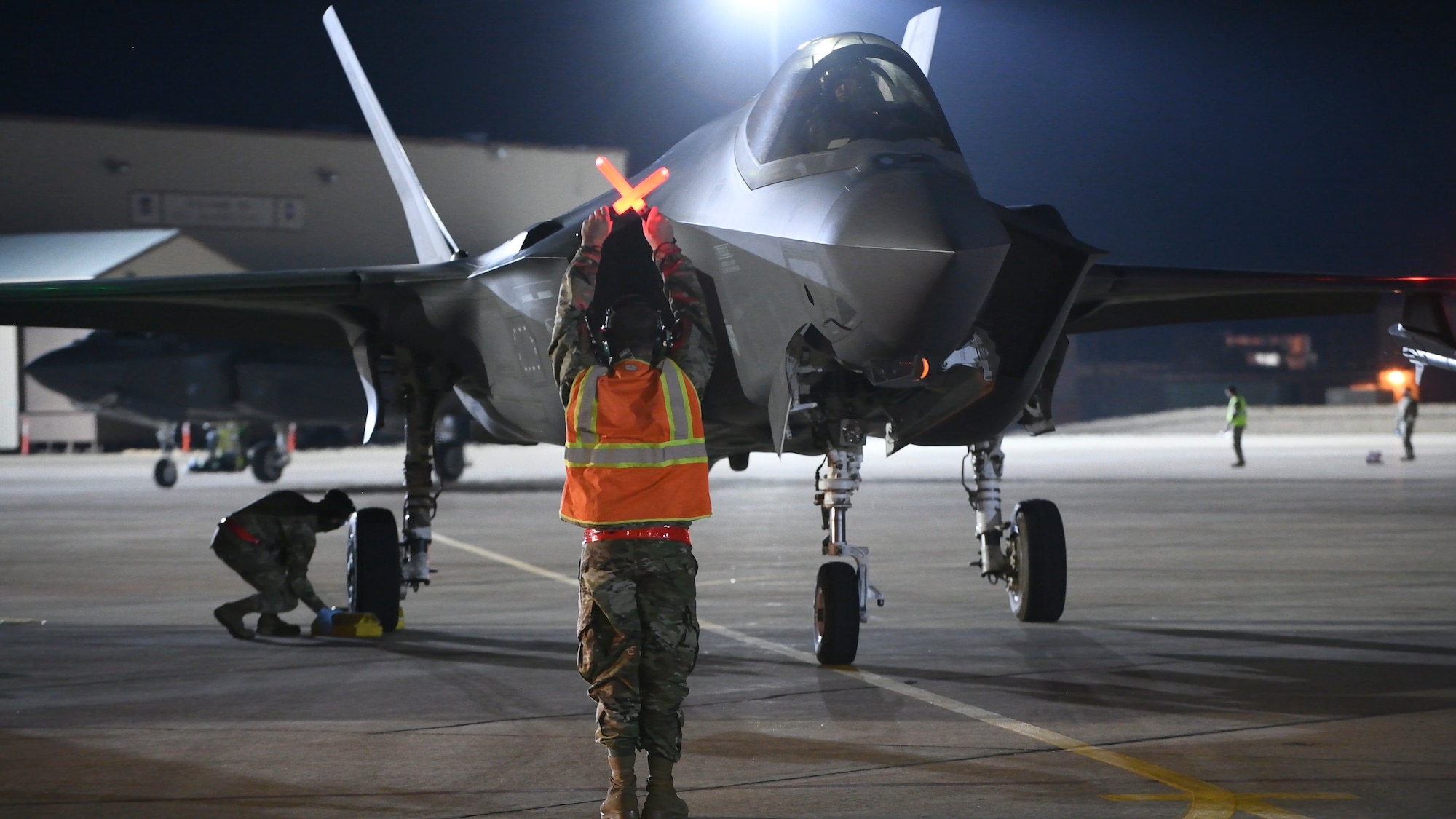 An Airman directs an F-35A Lightning II pilot to stop for a hot pit refuel with the aid of marshalling wands