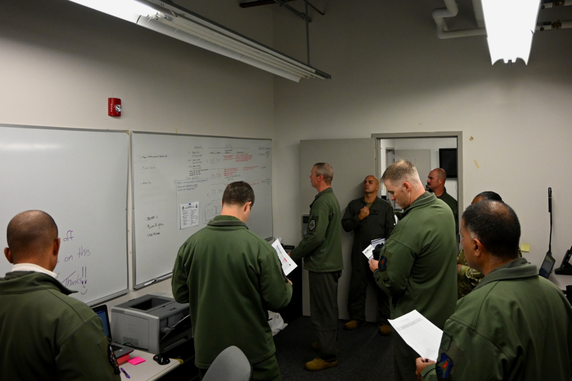 Airmen gather around a white board during a briefing.