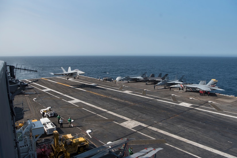 A fighter jet lands on the deck of an aircraft carrier as it sails on the ocean.