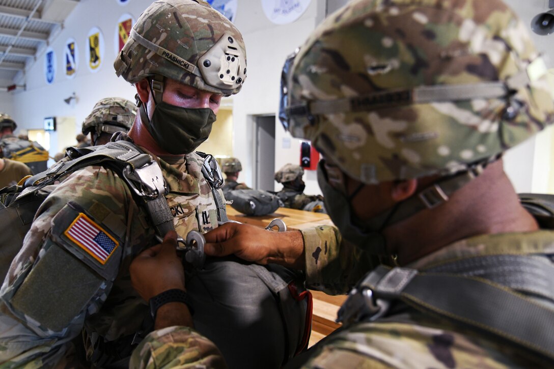 Two Army soldiers wearing face masks prepare their parachutes.
