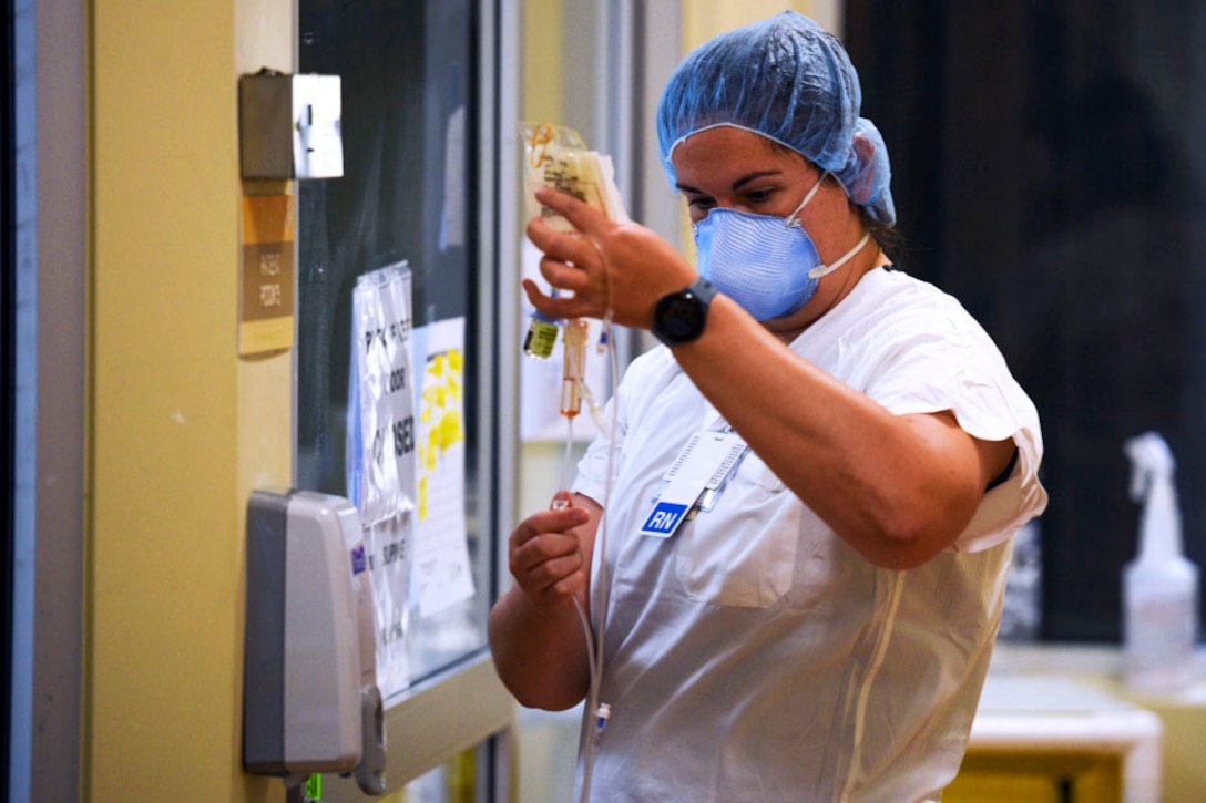 A nurse wearing a mask replaces an intravenous drip line.