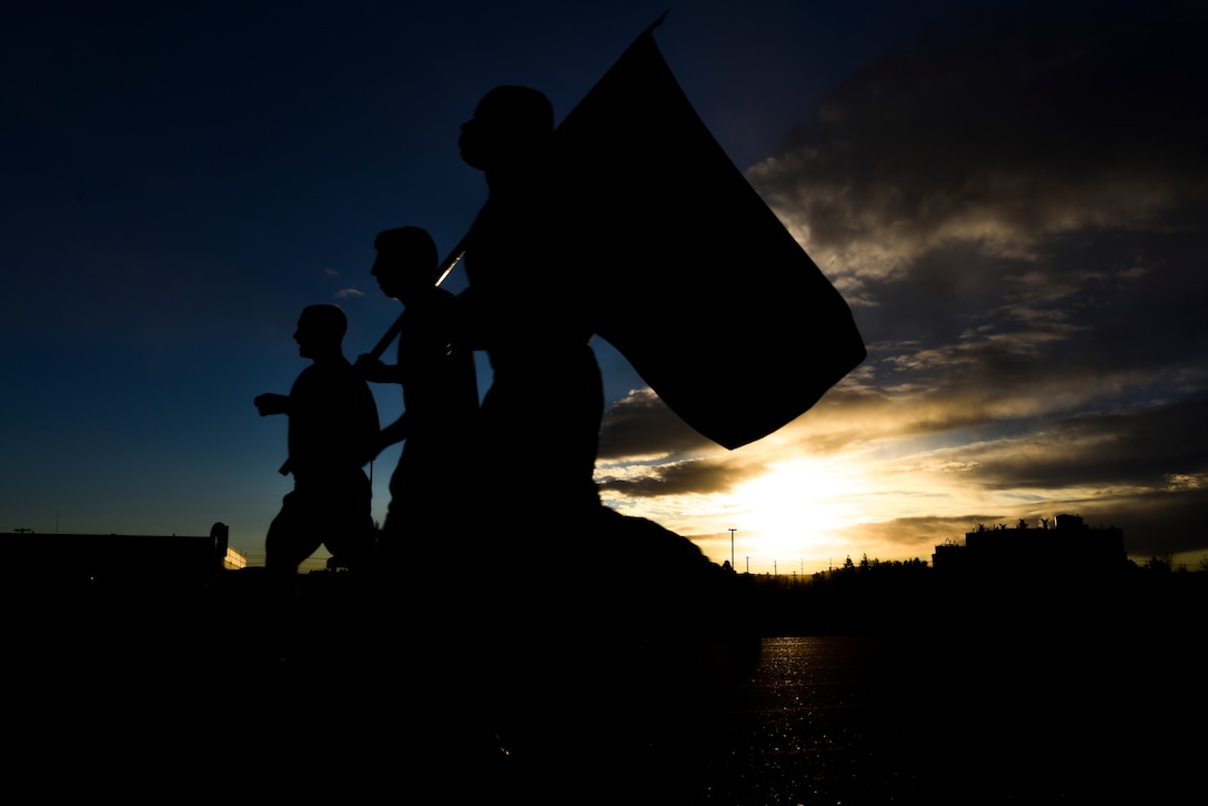 Three runners in silhouette run along a track carrying a flag.