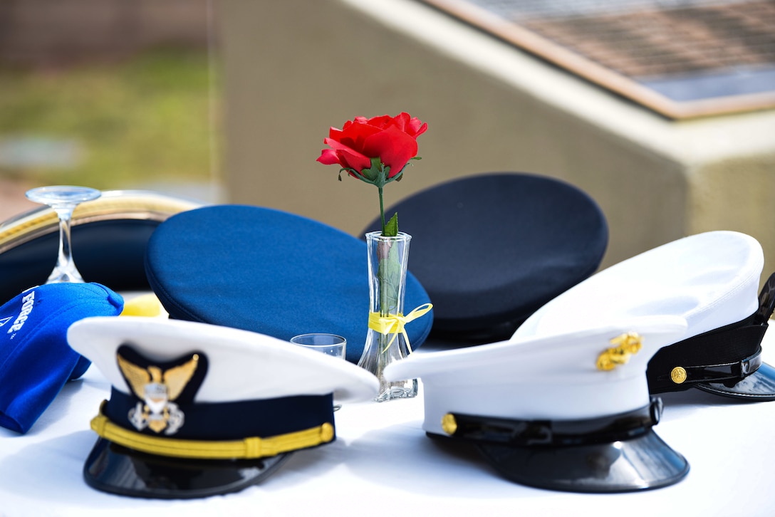 A group of military hats and a rose in a vase sit on a table.