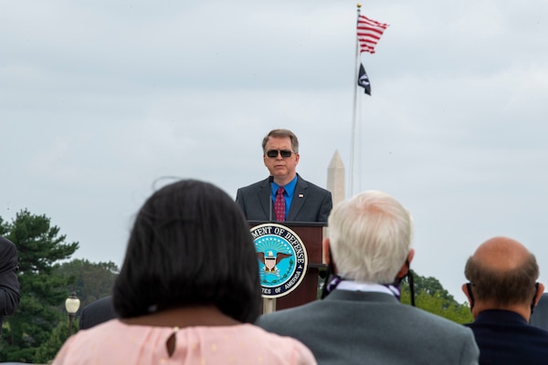 The deputy secretary speaks at at a podium to an audience outdoors.