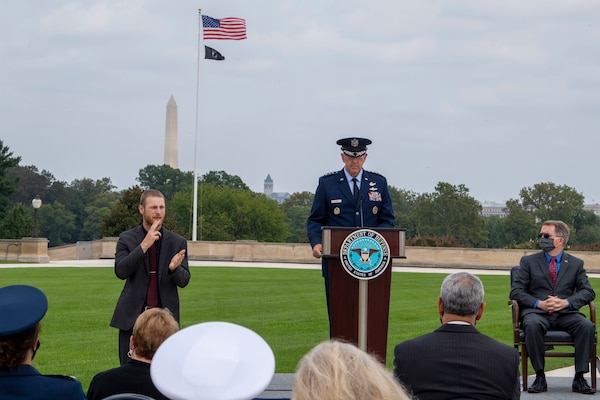 The voice chairman stands at an outdoor podium and speaks to an audience.