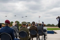 Attendees sit during an outdoor ceremony while aircraft fly overhead.