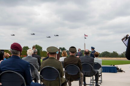 Attendees sit during an outdoor ceremony while aircraft fly overhead.