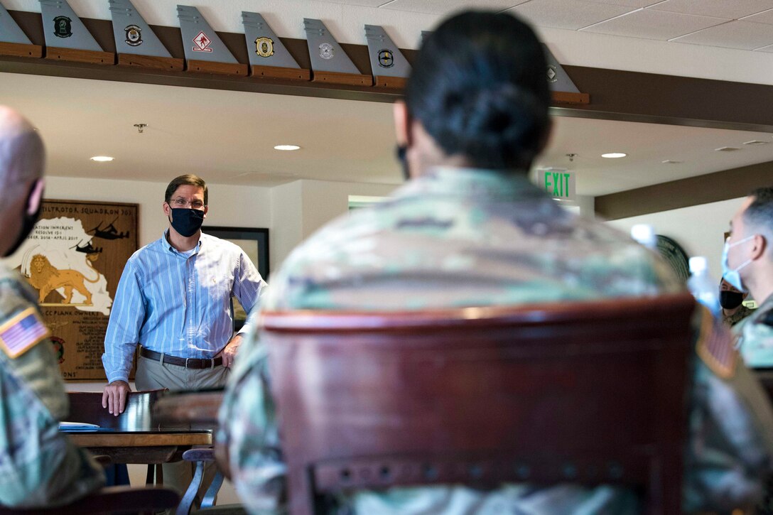 Defense Secretary Dr. Mark T. Esper stands in front of a group of sitted service members.