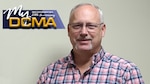 Man wearing striped shirt stands against a wall with the My DCMA logo placed in the upper left portion of the photo