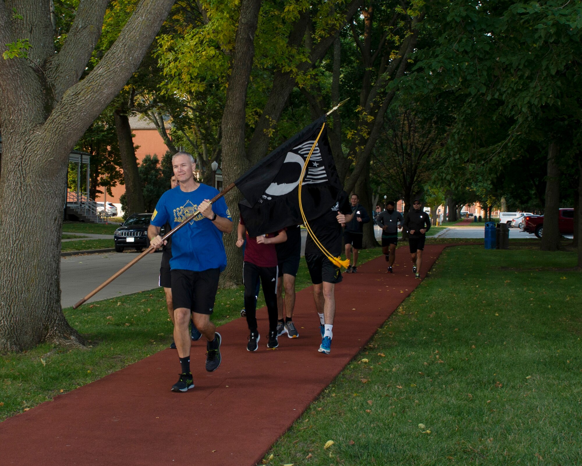 Command Chief  Brian Thomas running while carrying the POW/MIA flag, behind him a group of Airmen in civilian clothing