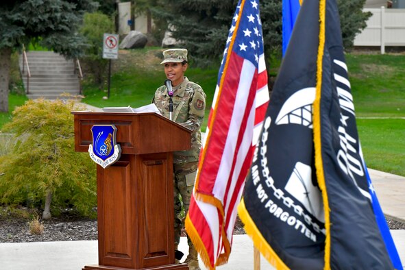 Presiding officer Col. Jenise Carroll, 75th Air Base Wing commander, addresses attendees from behind a podium next to the American and POW/MIA flags.