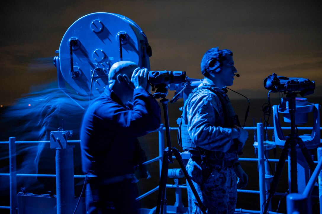 Sailors stand watch on ship at night.