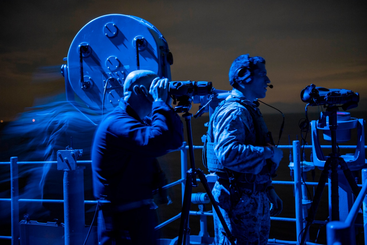 Sailors stand watch on ship at night.