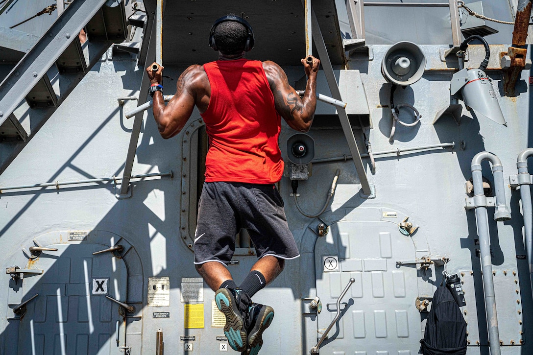 A sailor does pullups on a ship.