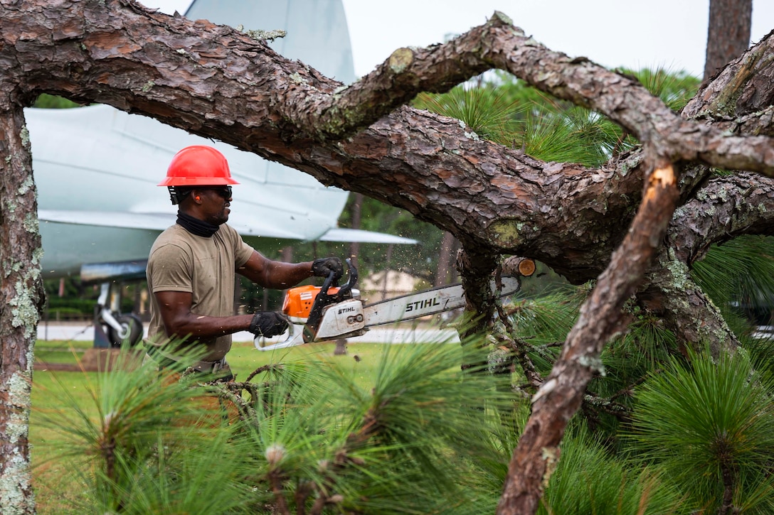 An airman uses a chainsaw to cut a fallen tree.