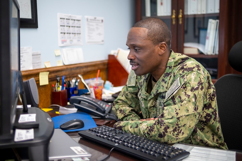 A man in a uniform works at a computer.