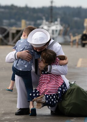 A Sailor assigned to the guided-missile destroyer USS Kidd (DDG 100) reunites with his children on the pier.