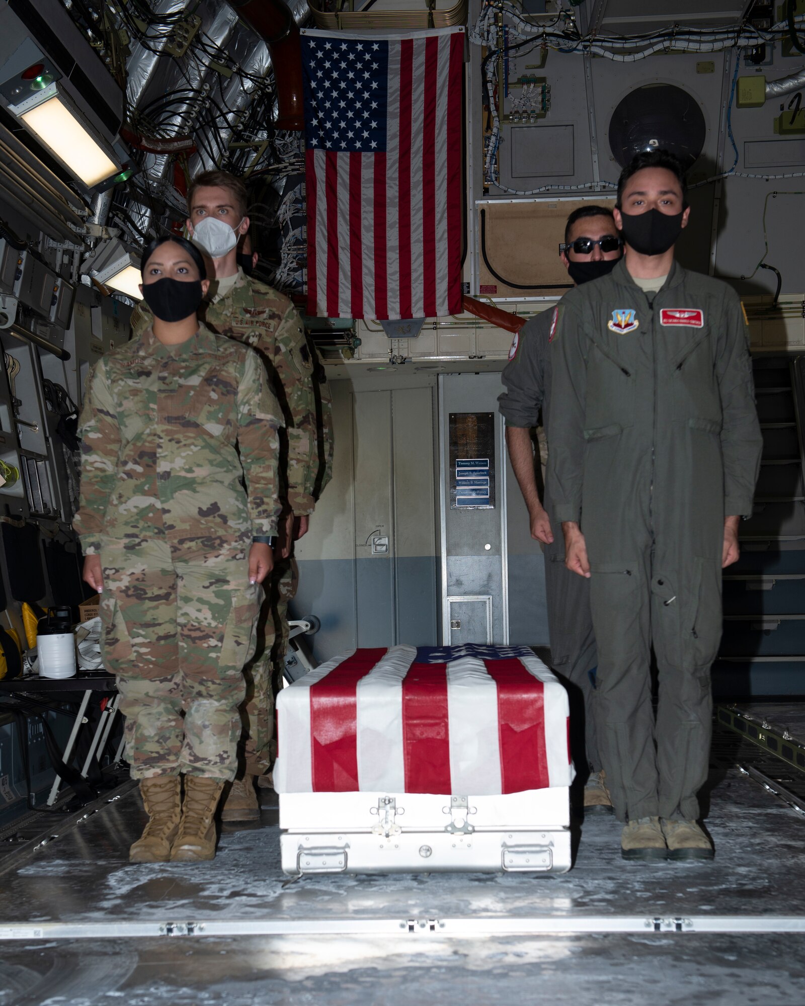 Airmen inside cargo area of airplane, standing at attention next to a U.S. flag draped transfer case