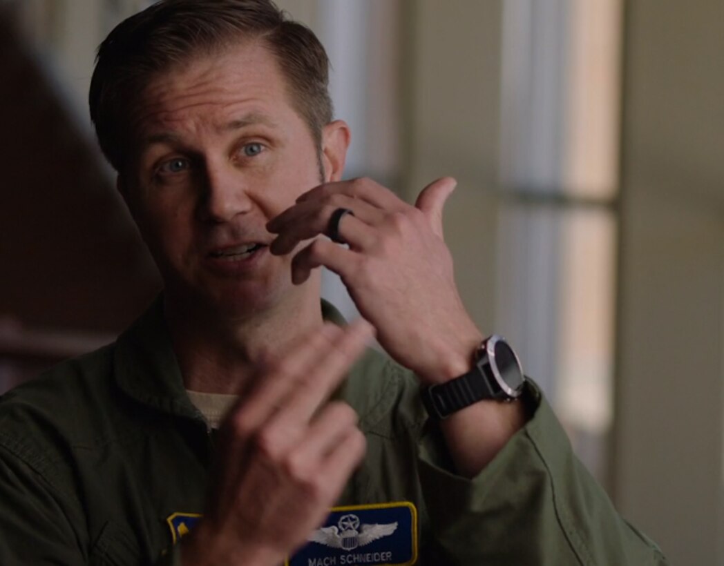 An airman man points to a watch on his wrist.