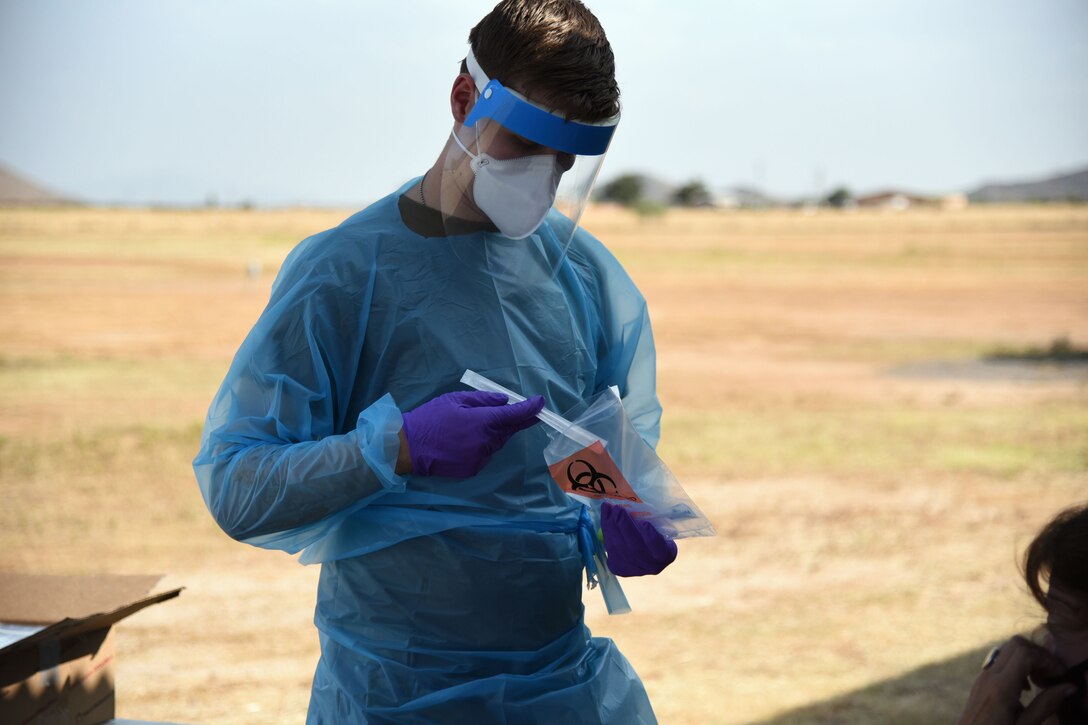 A soldier wearing personal protective equipment puts a vial into a plastic bag.