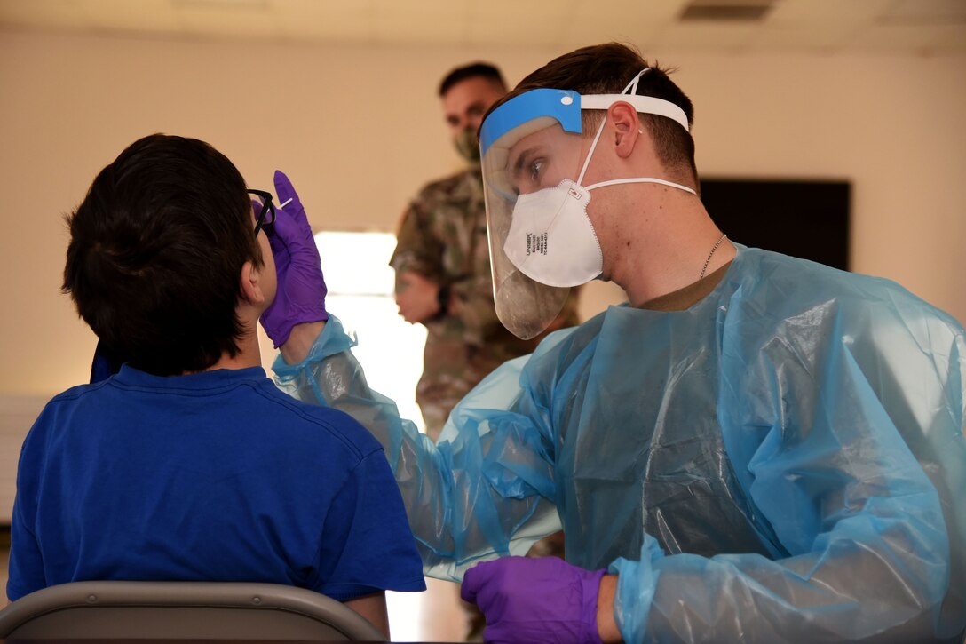 A soldier wearing personal protective equipment swabs a patient's nose.