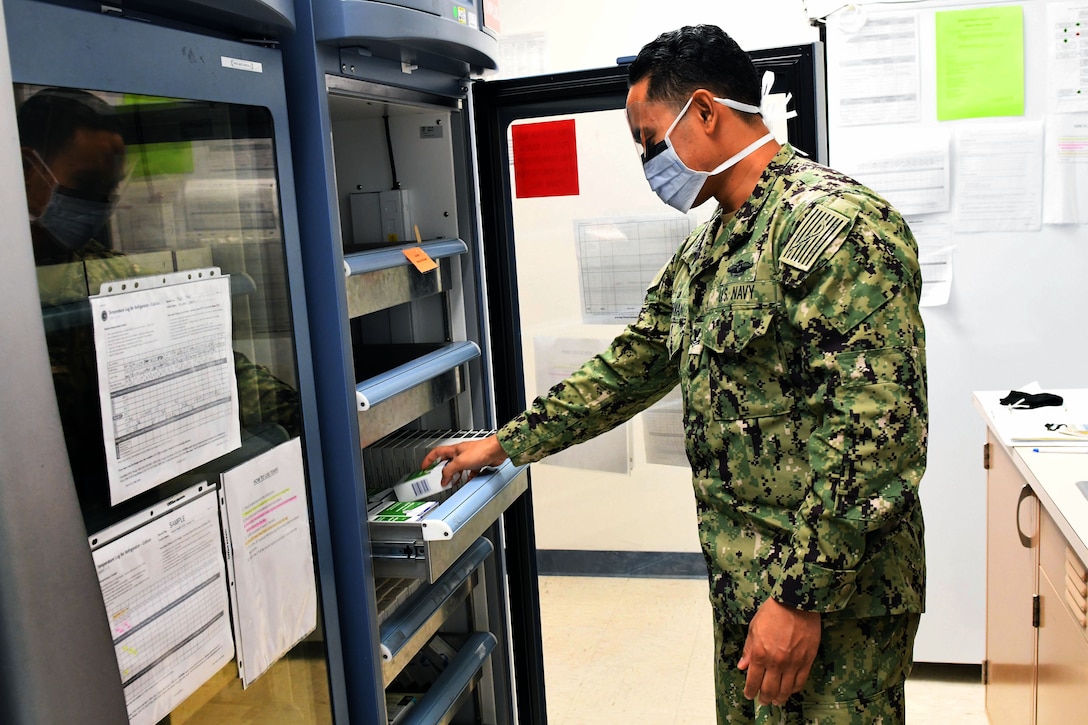A service member wearing a face mask takes something from an open drawer.
