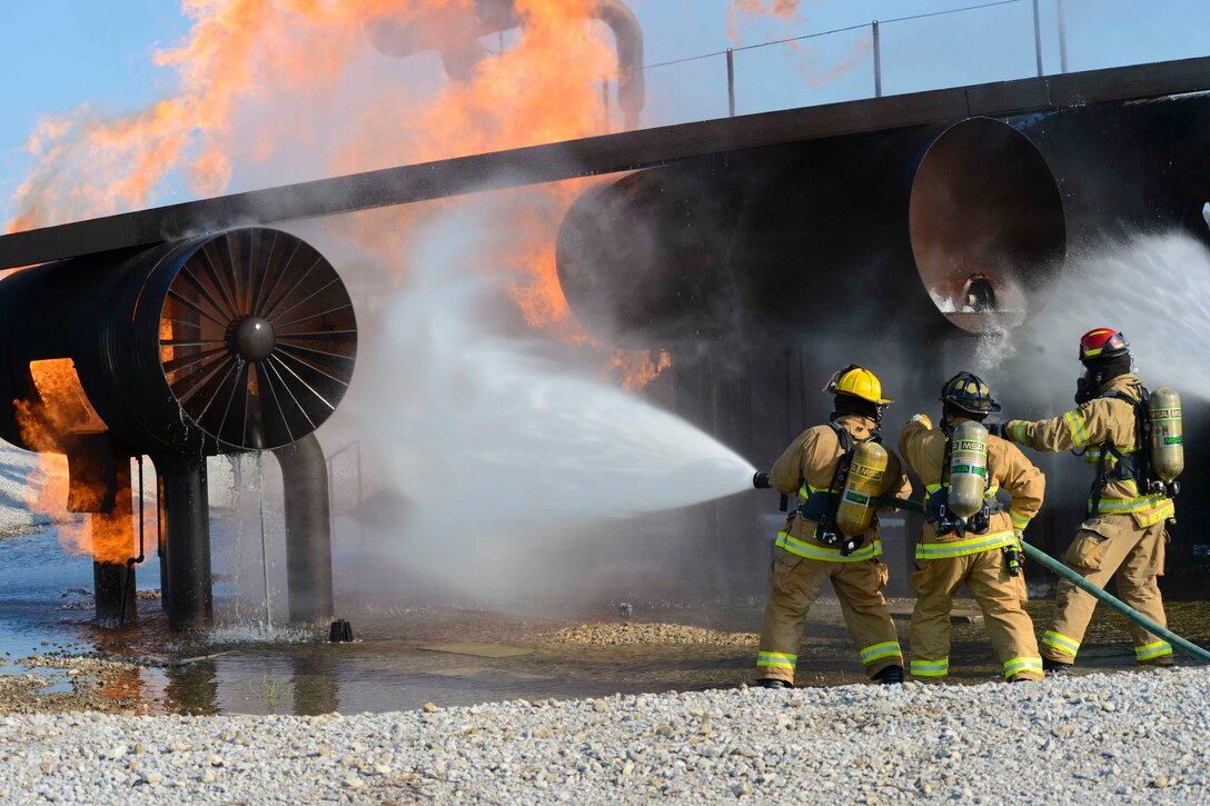 Three firefighters use a hose to spray water on a fire.