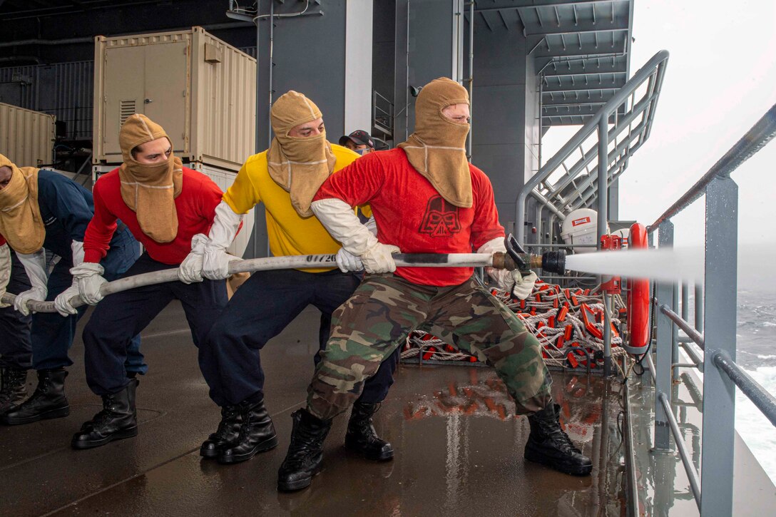 A group of sailors hold a fire hose as it sprays water.