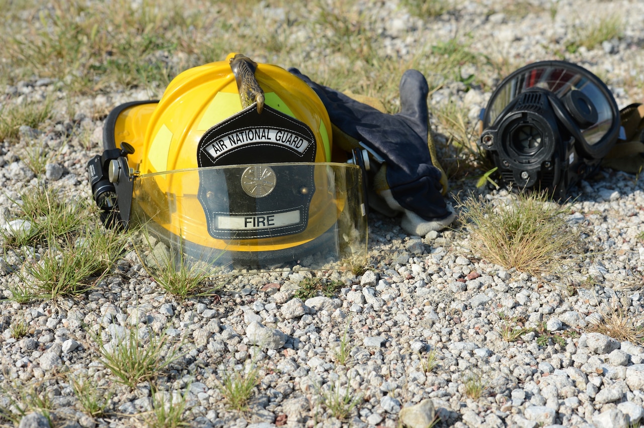 A yellow firefighter helmet sits on the ground next to other gear.