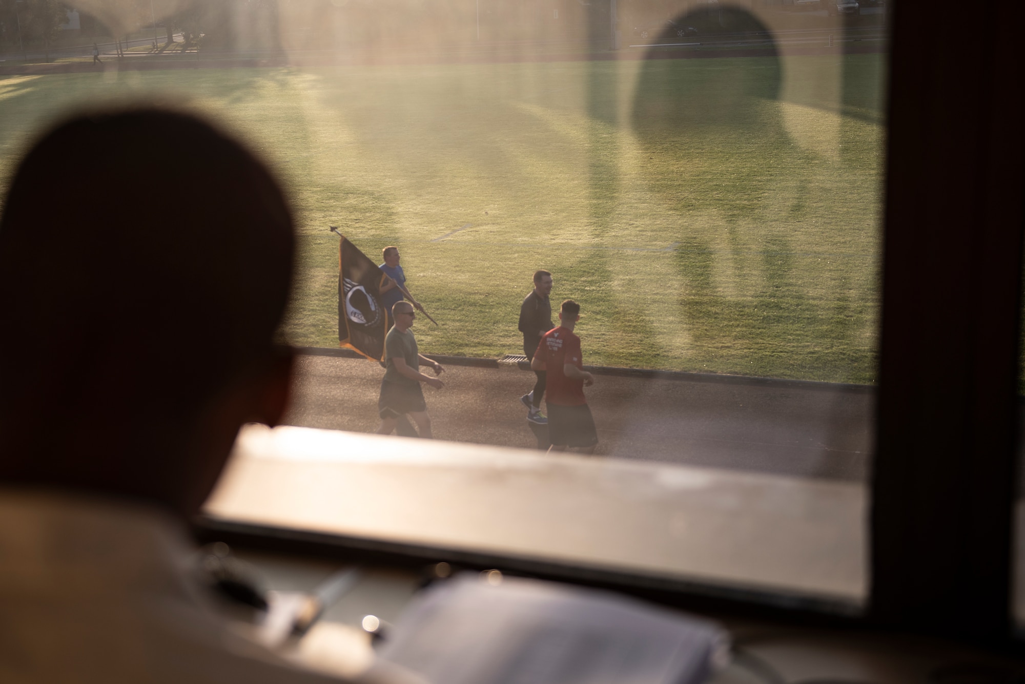 Airman 1st Class Christopher Williams reads names of service members listed as Prisoners of War and Missing in Action since WWII, as volunteers carry the POW/MIA flag on the track below, at Royal Air Force Lakenheath, England, Sept. 17, 2020. Members of the 48th Fighter Wing kept the flag in constant motion for 24 hours in honor of more than 82,000 Americans who were Prisoners of War and Missing in Action from past conflicts. (U.S. Air Force photo by Airman 1st Class Jessi Monte)