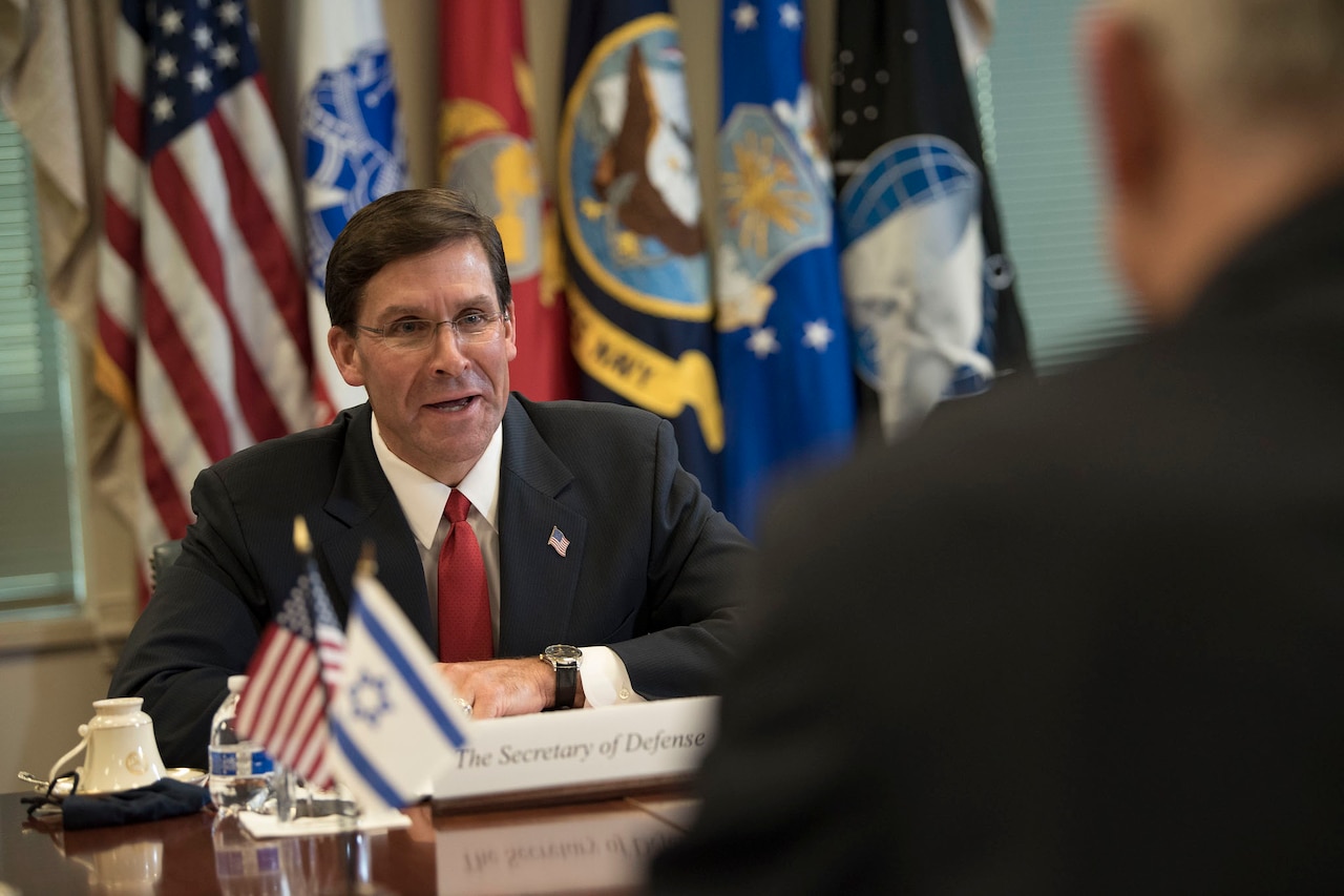 Defense Secretary Dr. Mark T. Esper speaks to another man sitting across from him at a table.