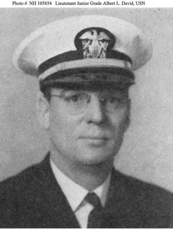 A man in a suit and Navy cap looks forward.