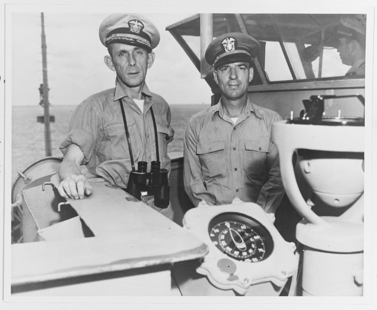 Two sailors pose for a photograph near the bridge of a ship.