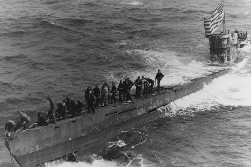 Several men stand on the topside of a partially submerged submarine that's flying a U.S. flag.