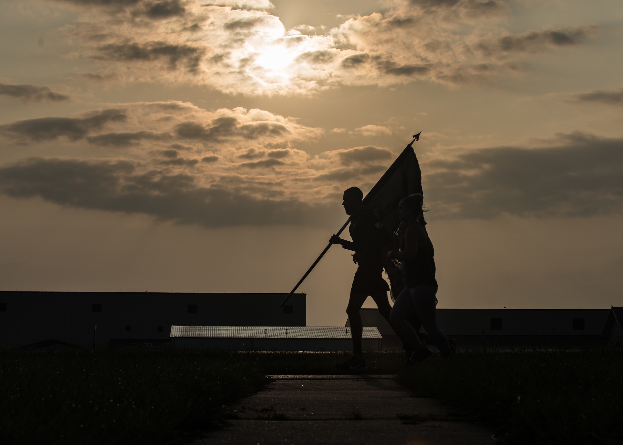 Airmen run with a POW/MIA flag next to the base lake.