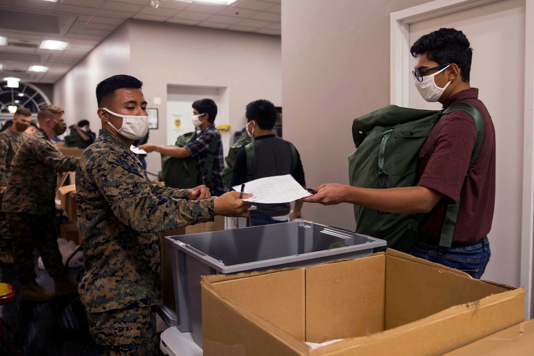 A new recruit wearing a face mask receives his initial gear from a soldier wearing a face mask.