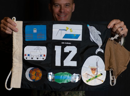 Cmdr. Mathias Vorachek, the commanding officer of USS Albany (SSN 753) holds a submarine battle flag created by his crew during a recent deployment.