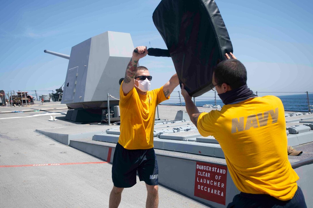 A sailor holds a punching bag as another sailor strikes it.