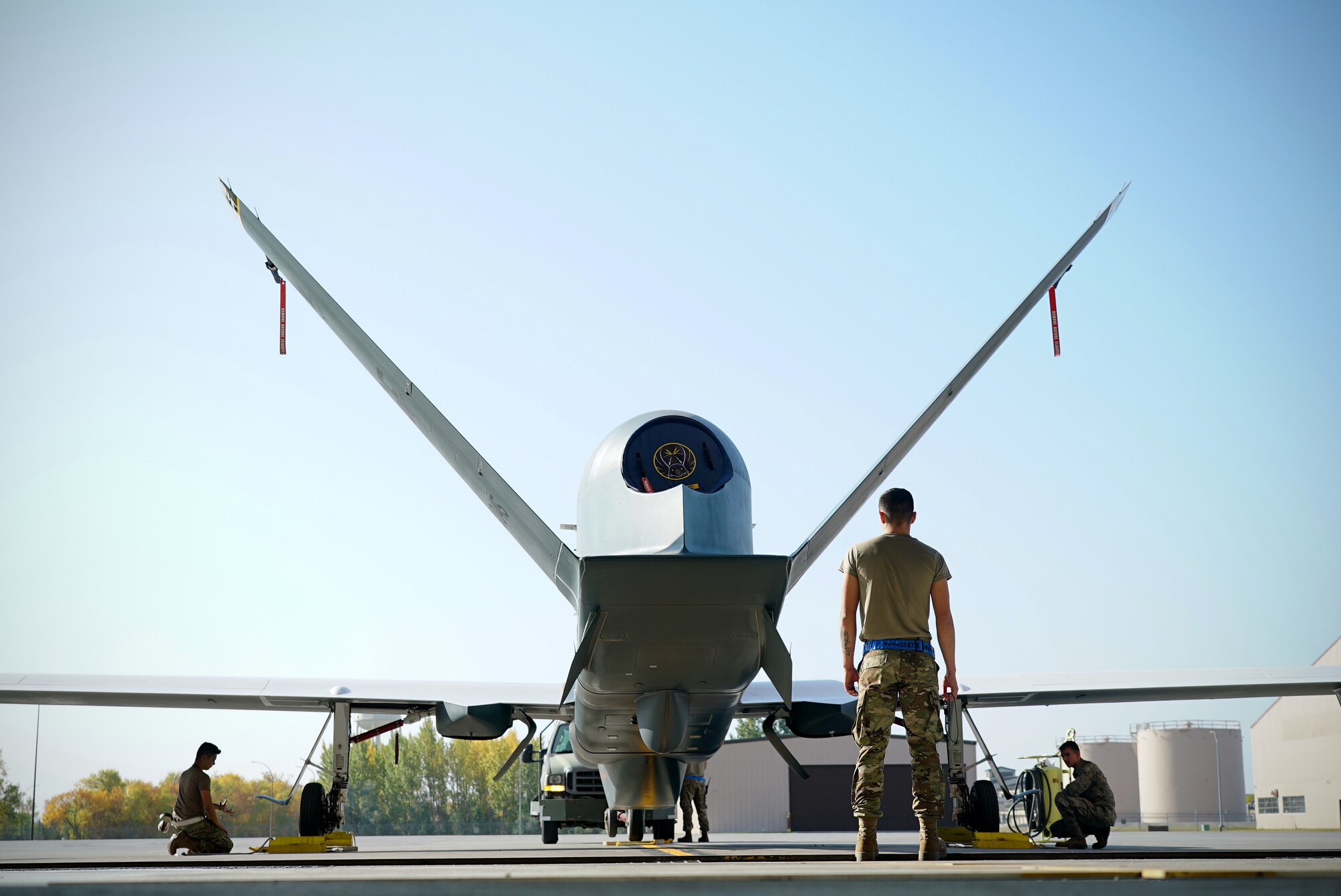 A uniformed military member stands with his back to the camera as he looks on to the back of a small unmanned aircraft.