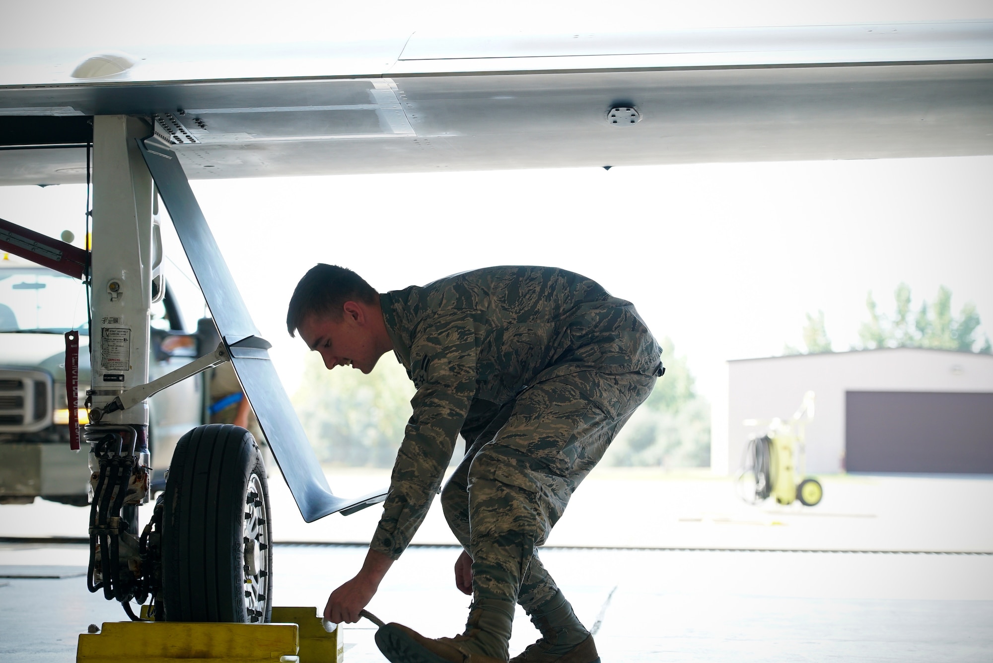 A man in military is shown center-frame leaning down to place chocks beneath an aircraft wheel.