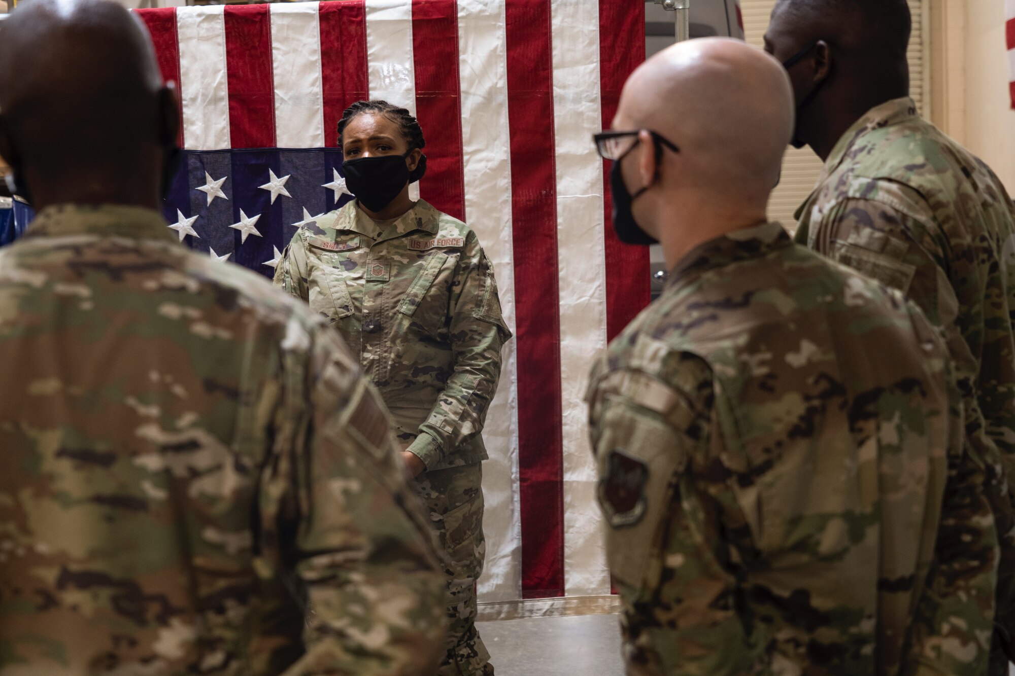 Woman in uniform in front of flag speaks to a group.